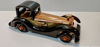Side view of handcrafted wooden vintage-style toy car showing body, fenders, roof and wheels