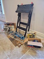 View of multiple tools including tile saw workbench, hand saw, jig saw in box, hand saw guide, and cardboard box with vise grip.