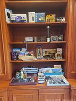 Photo showing the upper shelves of a wooden cabinet with various medical and office items including gloves, a flashlight, timers, a camera, and BlackBerry Q10 phone box.