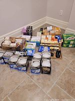 Wide view showing many different boxed lightbulbs arranged on floor in corner. Multiple brands and types visible.