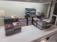 Photo showing stacks of DVDs, CDs, and cassette tapes arranged on a table, various titles visible
