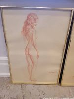 Sketched nude female figure standing in profile with back turned, framed with thin metallic border, signed by artist