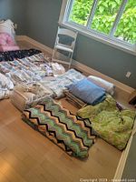 Overview of bed sheets, blankets, and a white folding chair arranged on the floor near a window.