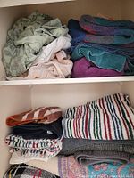 Closet shelf showing folded towels in various colors and patterns including green, purple, striped, and solid hues.