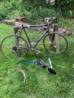Full side view of the Cannondale bicycle leaning on wooden rack. Accessories laid out on grass include pump, saddle bag, and partial tire rim.