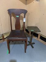 Wood dining chair with curved backrest and dark leather look padded seat next to wood plant stand