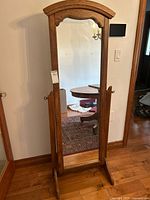 Front view of cheval mirror showing wooden frame, arched top, and full-length mirror reflecting room interior.