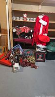 Full lot view showing Santa suit hanging, stockings on rack, assorted decorations laid on floor and stored in bins