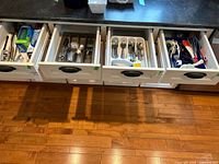 Four white drawers opened showing organized cutlery including spoons, forks, knives, and various kitchen utensils in trays.