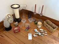 Wide-angle photo of all decor items arranged on floor showing glass candle holders, battery lantern, stained glass bird, shells, small print, wicker basket, and other decorative pieces.