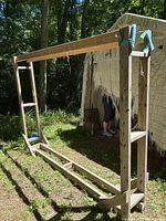 Wooden firewood storage holder frame outdoors in daylight with natural wood finish and visible structural braces.