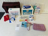 Photo of assorted first aid kits, ointments, bandages, tapes and carrying cases on white surface