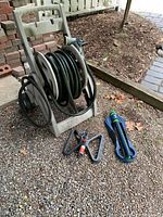 Photo showing wheeled reel with garden hose coiled, handheld spray nozzle and two sprinklers placed on ground