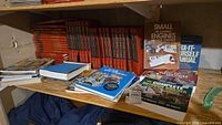 Shelf with various handyman instructional books including sets of Practical Handyman Encyclopedia, Popular Mechanics DIY Encyclopedia, and several paperback manuals focused on small engines and outdoor builder topics.
