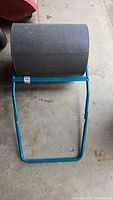 Full view of the lawn roller showing the large cylindrical roller and blue frame with handle.