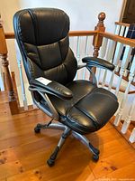 Front and angled side view of a black padded office chair showing the seat, backrest, armrests, and caster wheels.
