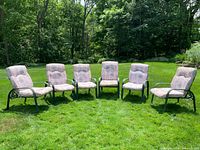 Six outdoor aluminum frame chairs with weathered cushions arranged on grass in daylight.