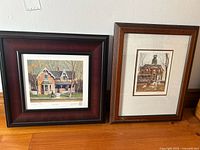 Two framed prints of houses shown side by side against a wall, one by A.J. Casson and one by Walter Campbell.
