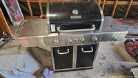 Full front angle of the Master Forge propane BBQ showing side burner with metal cover, control knobs, double-door storage, and handle on the lid