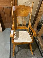 Front view of the wooden rocking chair showing decorative backrest, armrests, and cream seat pad.
