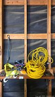 Shelf with yellow coiled extension cord and yellow tow line with hooks alongside various ropes and straps.
