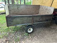 Side view of the utility trailer showing wooden panels, metal frame, and white-rimmed tires.