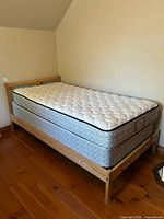 Full view of twin pine bed frame with mattress and box spring on wood floor against wall