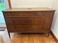 Front view of vintage wooden dresser showing 3 small drawers on top and 2 large drawers below, round metal ring handles, and turned legs. Shows wear and marks on surface.