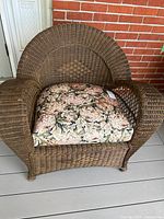 Front view of brown wicker chair with floral cushion, showing woven pattern and cushion detail.