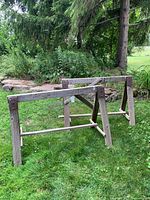 Pair of wooden workhorses placed on grass with garden background, showing general wear and structural details