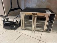 Gourmia air fryer and T-fal panini press on tiled floor, showing size and condition