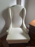 Front view of the cream-colored, wingback upholstered armchair with a high backrest and padded armrests.