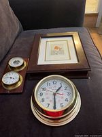 Lot items arranged on dark fabric: German barometer, framed bird print, Bulova clock, wooden key box