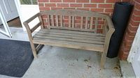 Front view of weathered wooden bench against brick wall showing slatted design and armrests.