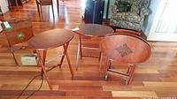 Set of four oval wood folding tables arranged together with a storage stand visible on hardwood flooring in a living room setting.