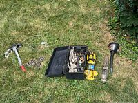 Wide shot showing trailer hitch, toolbox with tools, bottle jack, chain, and come along winch on grass surface.