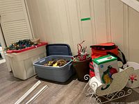 Photo showing multiple plastic bins filled with Christmas lights, ornaments, fall decorations, a decorative basket with red berries, an insulated bag, a box of Christmas lights, and a small white decorative sleigh.