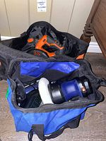 Top view showing black and blue Simoniz cordless polisher with wool pad and orange and black Black & Decker circular saw inside their respective soft tool bags.