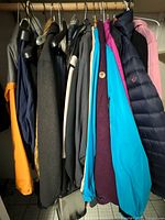 Wide view of hanging outerwear jackets showing variety of winter jackets, rain jackets in dark, blue, pink, and yellow colors.