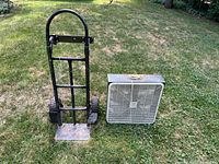 Photo showing the black metal frame hand cart dolly next to white rotor box fan on grass