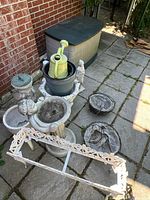 Photo showing Rubbermaid deck box, yellow watering can inside a planter, garden statues, planters, and decorative frame on paved patio.