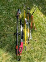 Full view of the five gardening tools laid on grass including pole saw, pole pruners, and clippers.