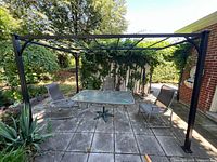Wide view of the entire metal gazebo frame set on a patio with some chairs and table inside. Frame is black painted metal with noticeable wear and rust.