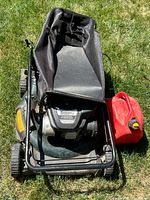 Top-down view of the Bolens MTD lawn mower with fabric grass catcher and red gas can next to it on grass.