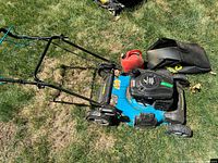 Full side view of the blue Yardworks lawn mower on grass showing handlebar, wheels, and grass catcher bag beside it.
