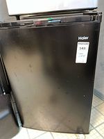 Black Haier mini bar fridge front closed view with visible wear and scratch marks.