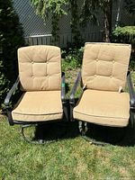 Two metal outdoor swivel chairs with beige cushions set on grass in sunlight