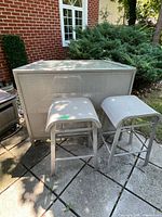 Front view of metal patio bar and two matching stools outdoors on stone patio.