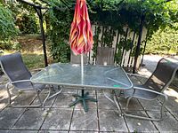 Photo showing full patio set with four chairs, rectangular glass table, and folded umbrella with stand.
