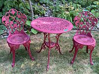 Full view of red painted cast iron patio table with matching chairs placed on grass outdoors